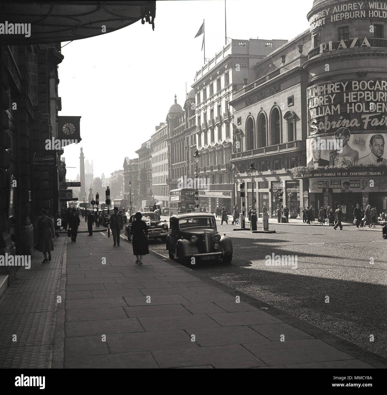1954, historical, a view down Lower Regent Street from Piccadilly Circus, Westminster, London, England. The Plaza cinema (theatre) is on the right. Built for Paramount Pictures in 1926, the Plaza was a lavish building with seating for 1800 and a small stage. Advertised on its' exterior some of the greatest names in the movie world, Humphrey Bogart, Audrey Hepburn and William Holden, who were starring in the comedy-drama film 'Sabrina Fair', directed by  Billy Wilder.  The American made film was a Paramount Production Stock Photo