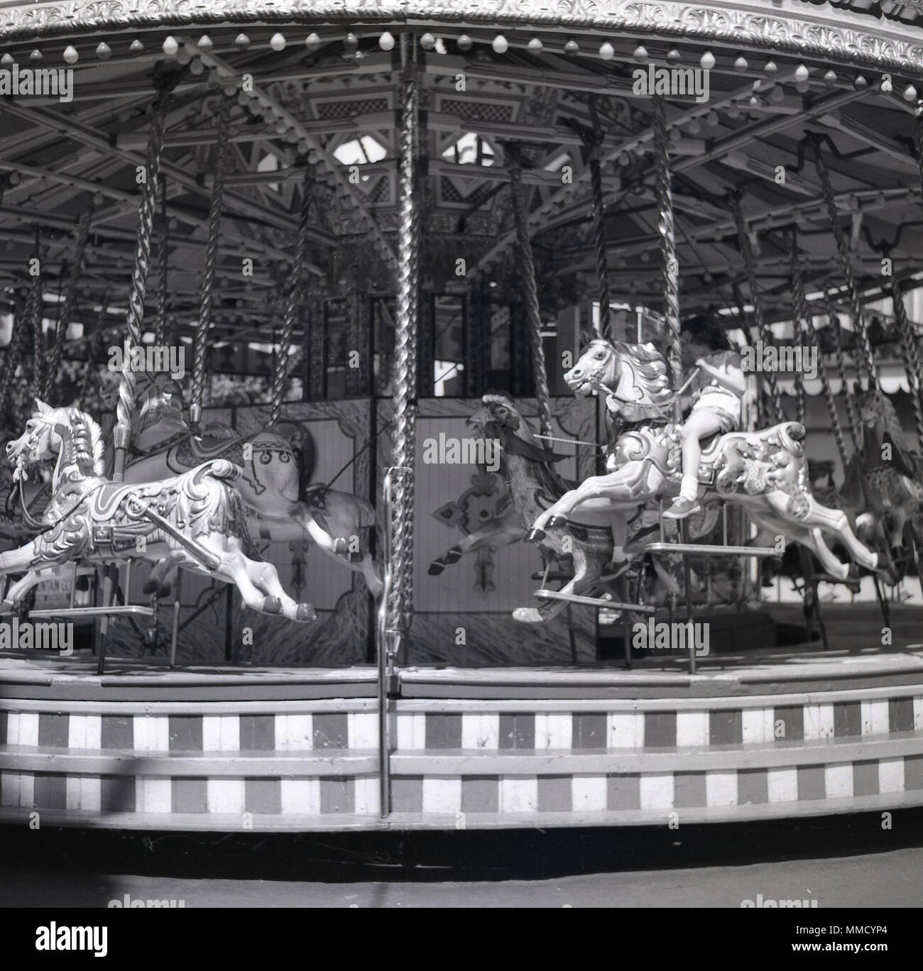 1960s, historical, young girl riding a wooden horse on a carousel or merry-go-round at the fun fair at Battersea Park, London, England, UK. The fairground was built for the 1951 Festival of Britain celebrations in the nothern section of the park and was a major attractions for many years. Stock Photo