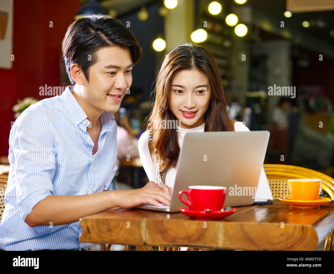 happy young asian couple sitting in coffee shop using laptop computer together. Stock Photo
