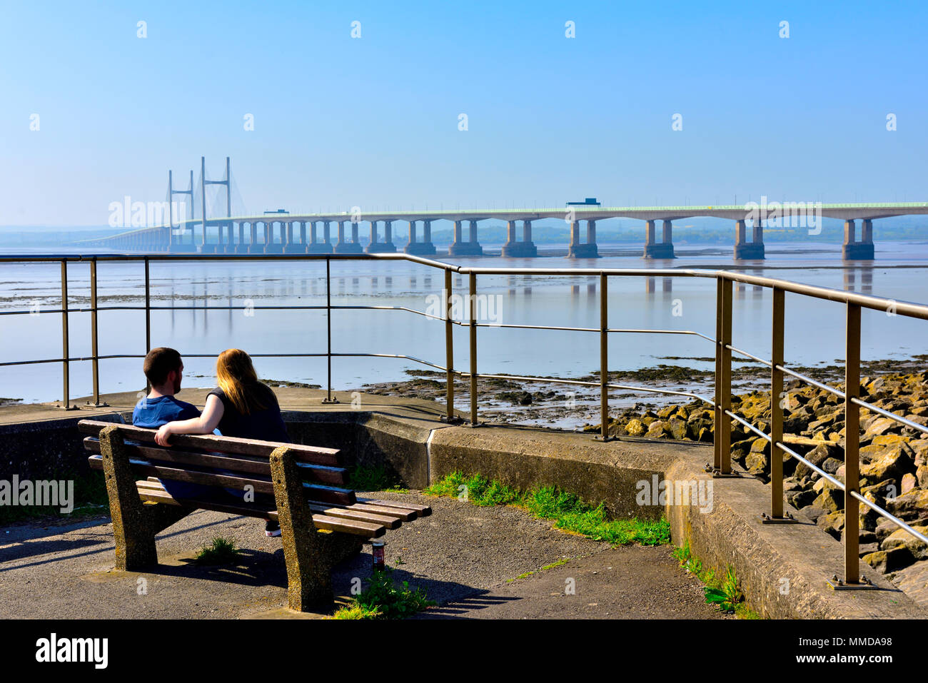 Two people on seat overlooking Severn Estuary with M4, Second Severn Crossing bridge Stock Photo
