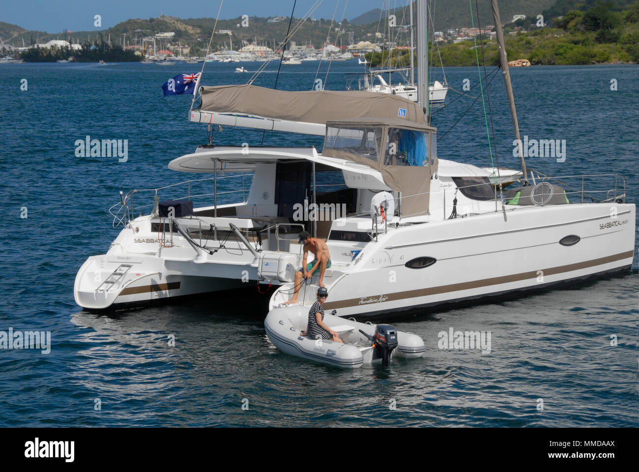 Young couple launching/retrieving inflatable dinghy with outboard motor from white catamaran, Simpson Bay, St Martin, Caribbean Stock Photo