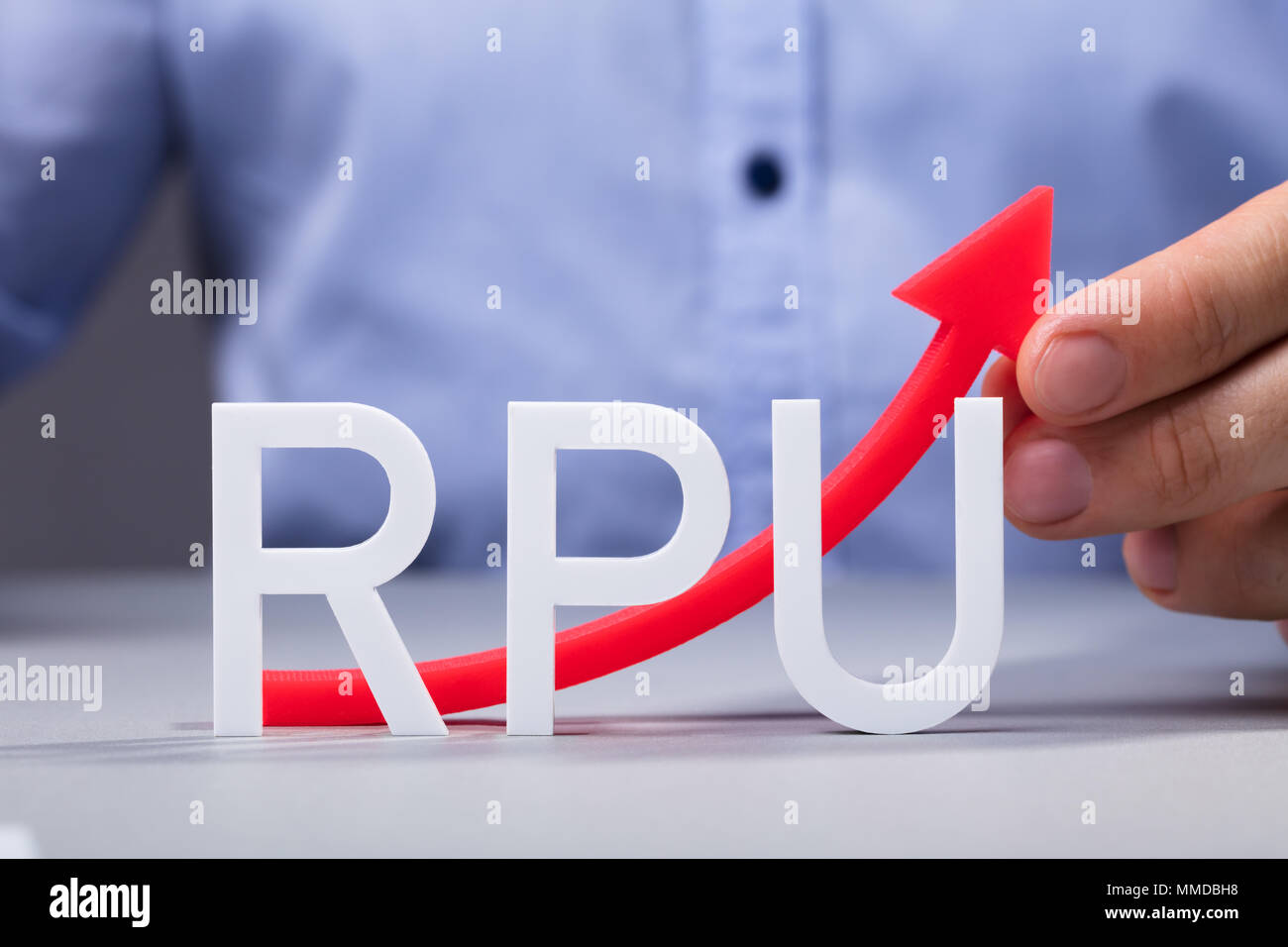 Businessman Holding Red Increasing Arrow Of Revenue Per User On Office Desk Stock Photo