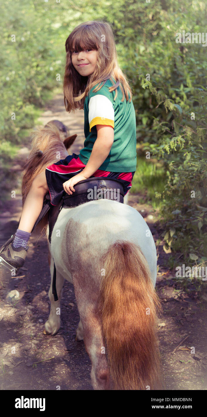 Beautiful Girl Child Riding into Woods on Miniature Horse Stock Photo