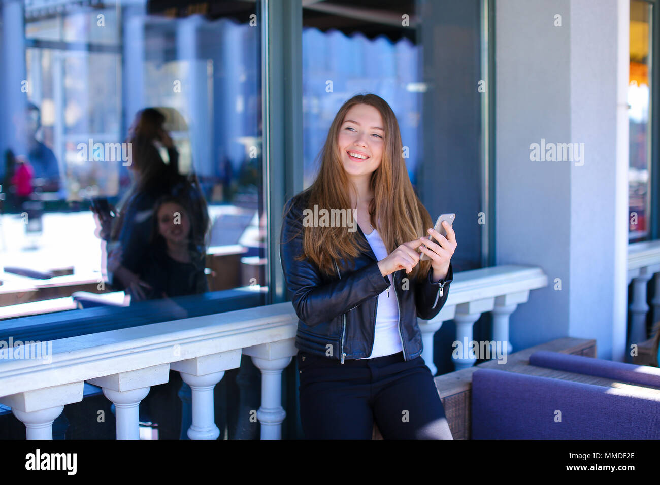 Jocund girl typing message by smartphone at street cafe. Stock Photo