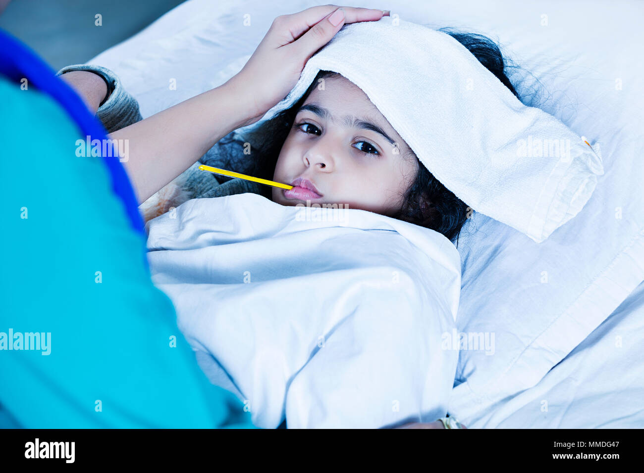Sick Girl with high fever laying in bed and mother taking temperature Stock Photo