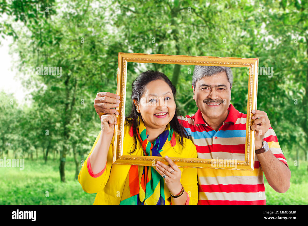 Happy Two Senior Couple holding picture frame Over face. In Garden Stock Photo