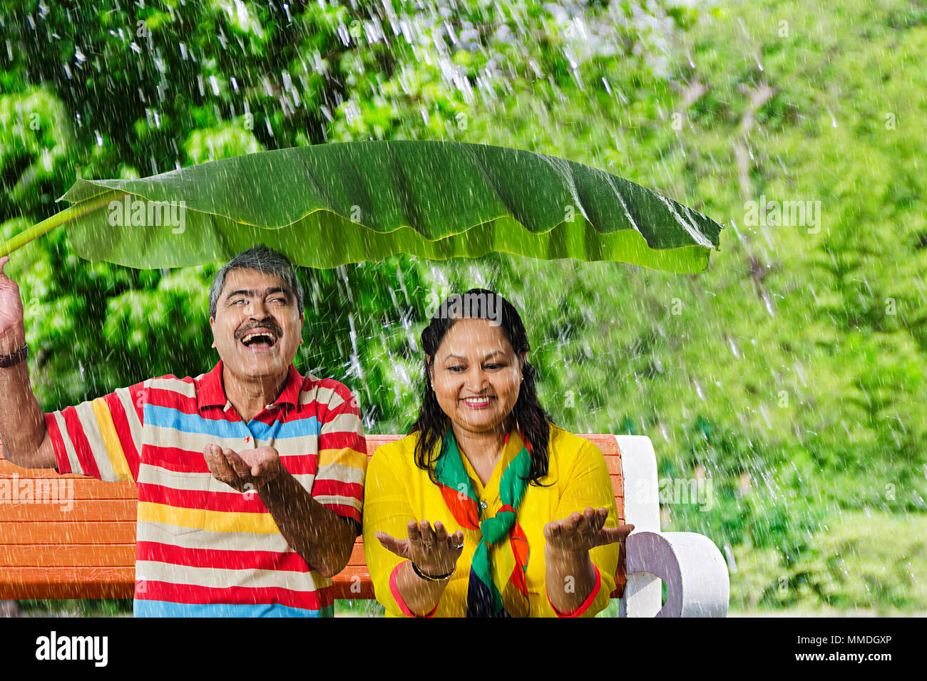Happy Old Couple Sitting Bench Park Under Banana-Leaves Rain. Enjoy Stock Photo
