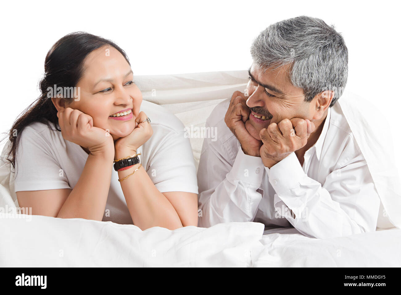 Happy Senior Couple Lying On Bed Looking-at-each-other Bedroom At-Home Stock Photo