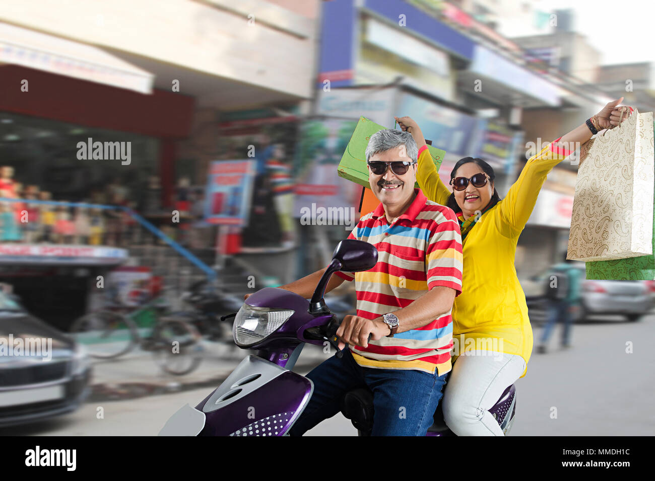 Happy Senior couple rides scooter With Shopping Bags on City-road Stock Photo
