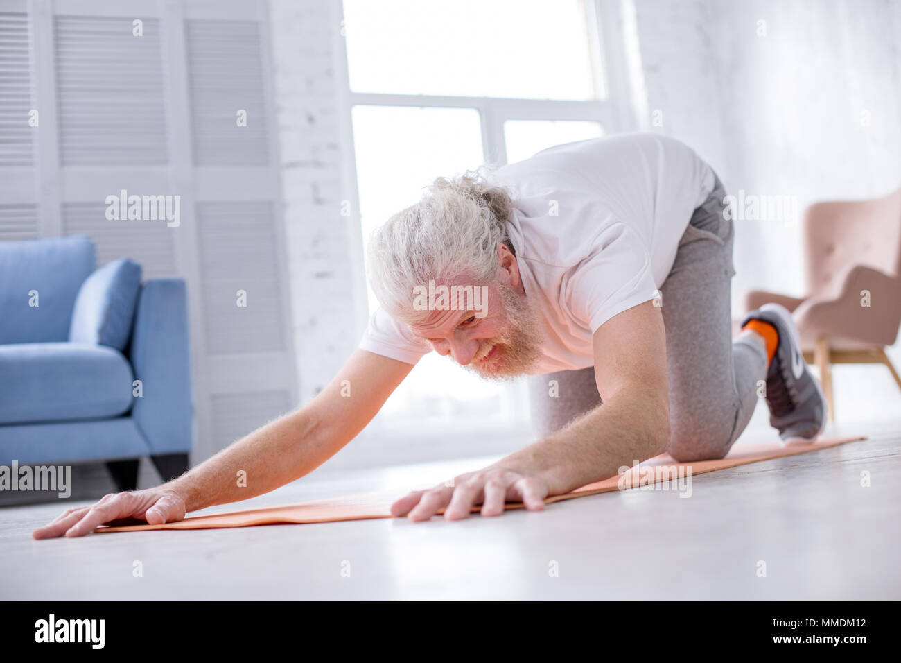Grey-haired senior man practicing extended puppy pose at home Stock Photo