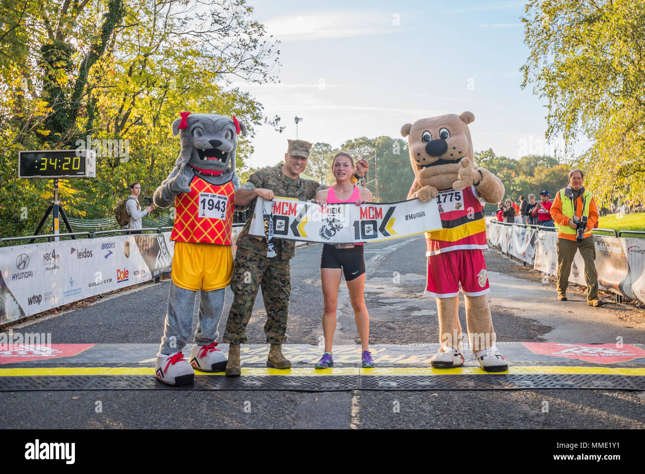 Sarah Bishop, Fairfax, Va., first female finisher of the Marine Corps Marathon (MCM) 10K, and U.S. Marine Corps Col. Joseph Murray, commanding officer of Marine Corps Base Quantico, pose for a photo with the MCM mascots, Arlington, Va., Oct. 22, 2017. Also known as 'The People's Marathon,' the 26.2 mile race drew roughly 30,000 participants to promote physical fitness, generate goodwill in the community, and showcase the organizational skills of the Marine Corps. (U.S. Marine Corps photo by Lance Cpl. Yasmin D. Perez) Stock Photo