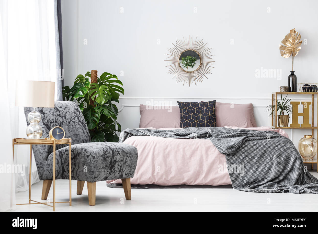 White hotel bedroom interior with pink, gray and gold accents such as a  mirror, armchair or table Stock Photo - Alamy