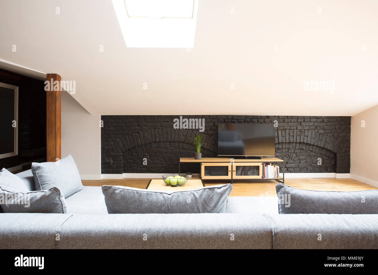 Television on black, brick wall standing in front of a grey couch in modern living room interior Stock Photo