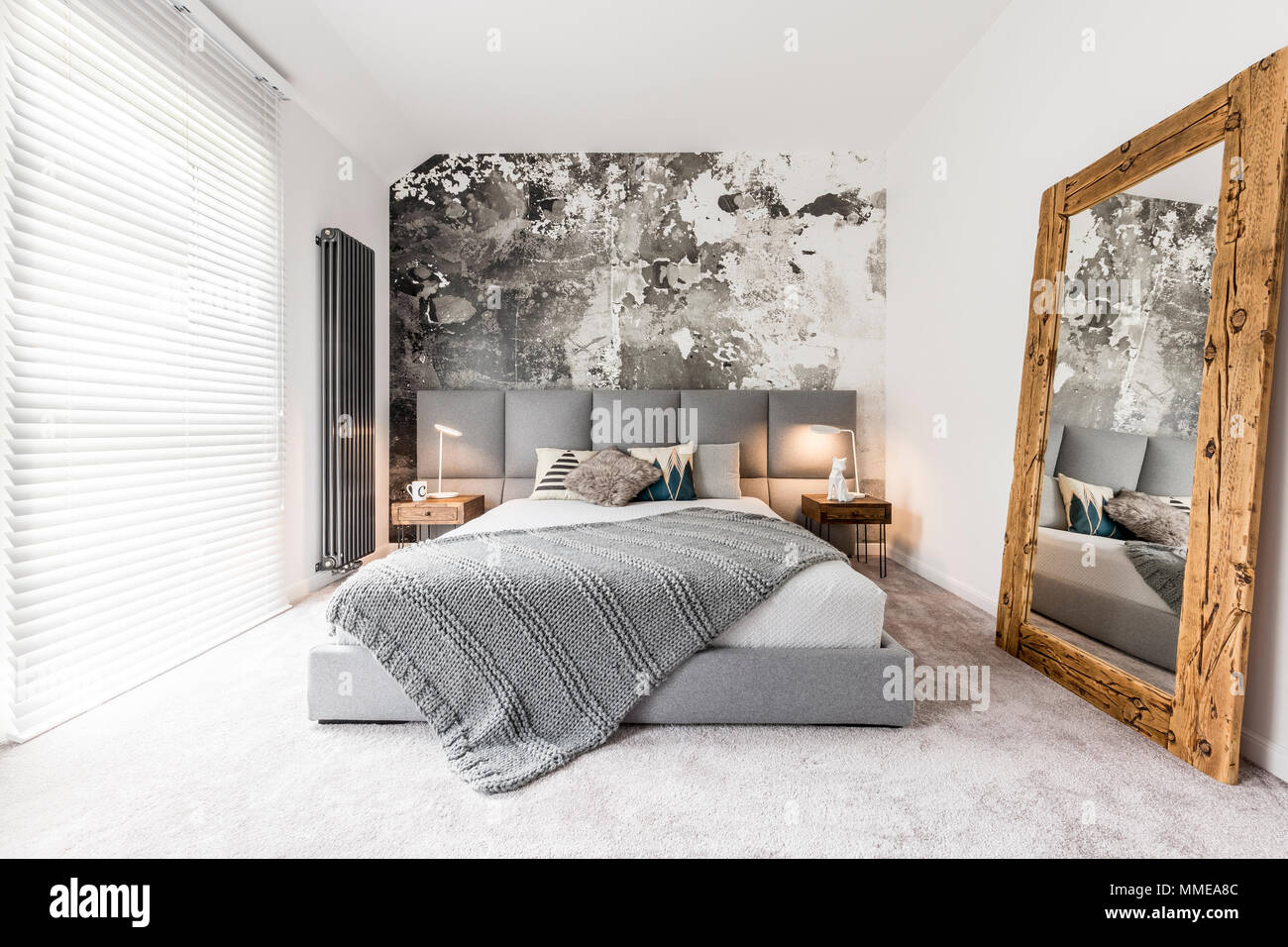 Kingsize bed with gray square headboard, large rustic wooden mirror and textured wall in trendy
