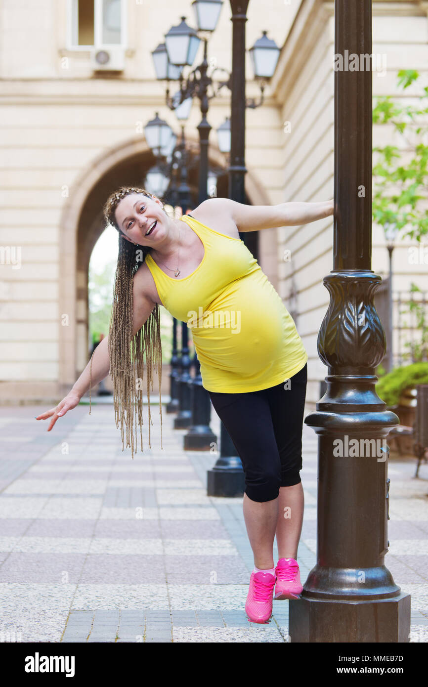 Smiling happy pregnant woman is playing on a street pole. Stock Photo