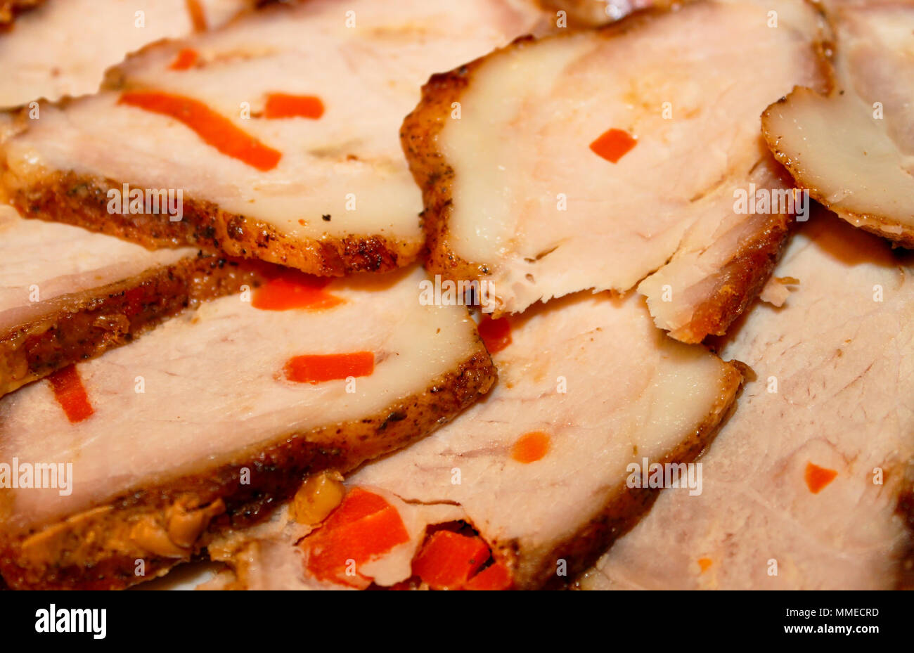 Sliced baked ham, stuffed with carrots and spiced spread out on a plate close up as background Stock Photo