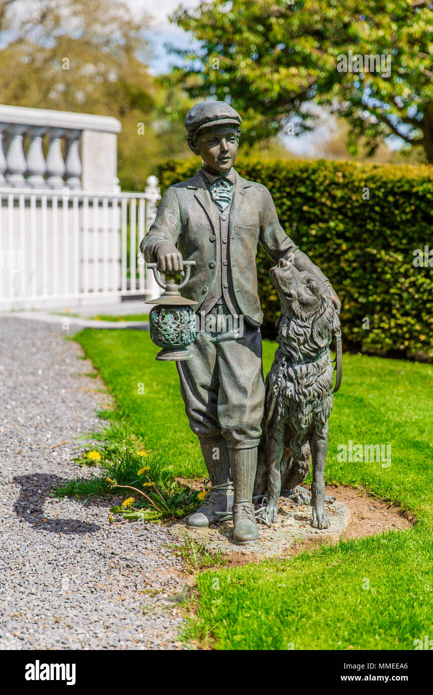 Garden statue of a boy holding a lantern with a dog at the Manor House in Palmerstown House Estate in Johnstown, County Kildare, Ireland Stock Photo