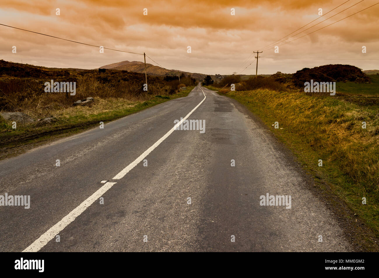 Straight empty road in the irish landscape under storm clouds with the evening light casting shadows. Stock Photo