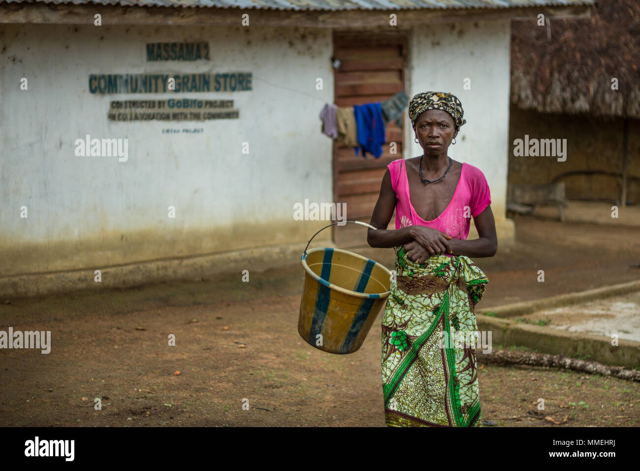 YONGORO, SIERRA LEONE - June 06, 2013: West Africa, unknown woman with a bucket next to the grain warehouse in the village of huts near the capital Fr Stock Photo