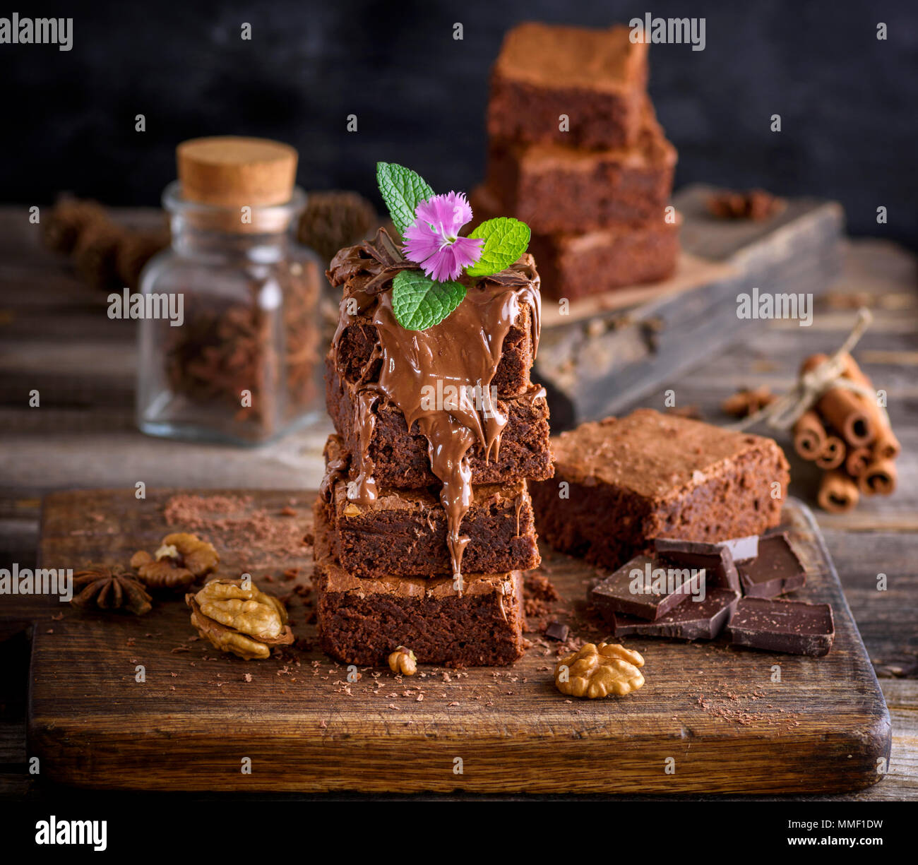 a stack of baked Brownie pie on a brown wooden board, a dessert is poured with a thick layer of chocolate and decorated with mint leaves and a flower Stock Photo