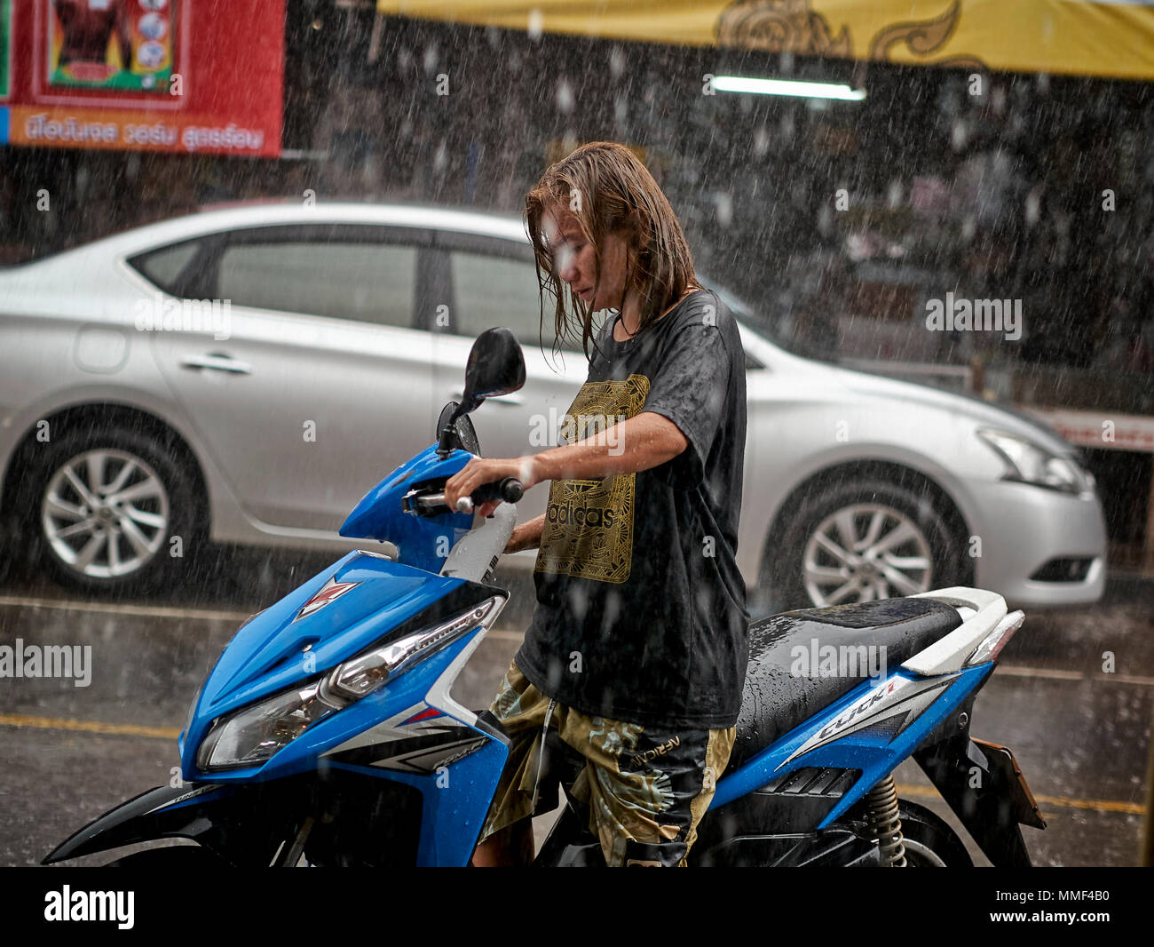 Rain. Woman with motorcycle caught in torrential rainfall. Thailand monsoon season. Southeast Asia. Stock Photo