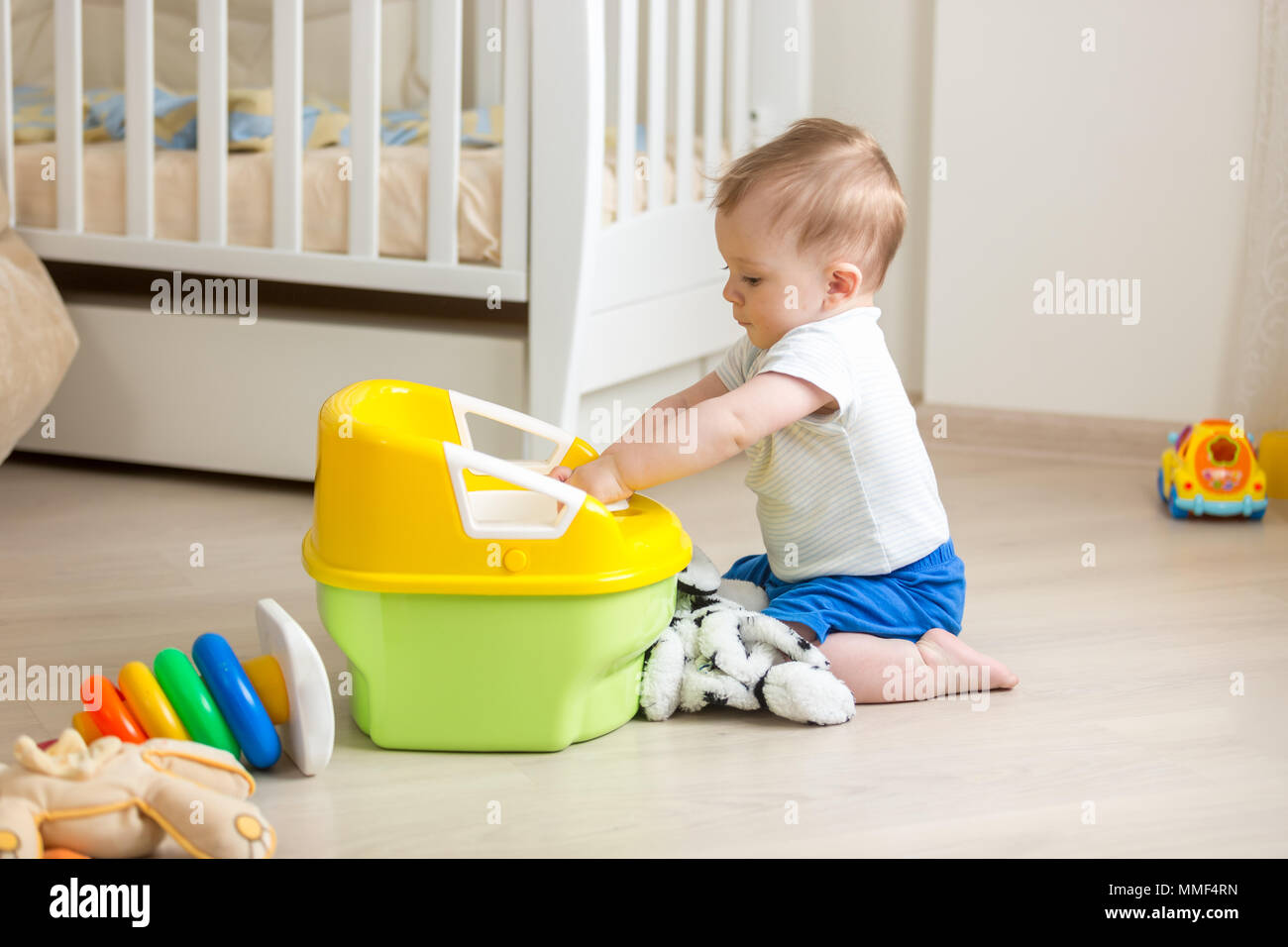 10 months old toddler boy sitting on floor and playing plastic toilet pot Stock Photo
