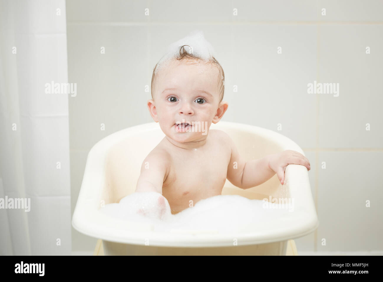 Portrait of 10 months old baby boy sitting in bath with foam Stock