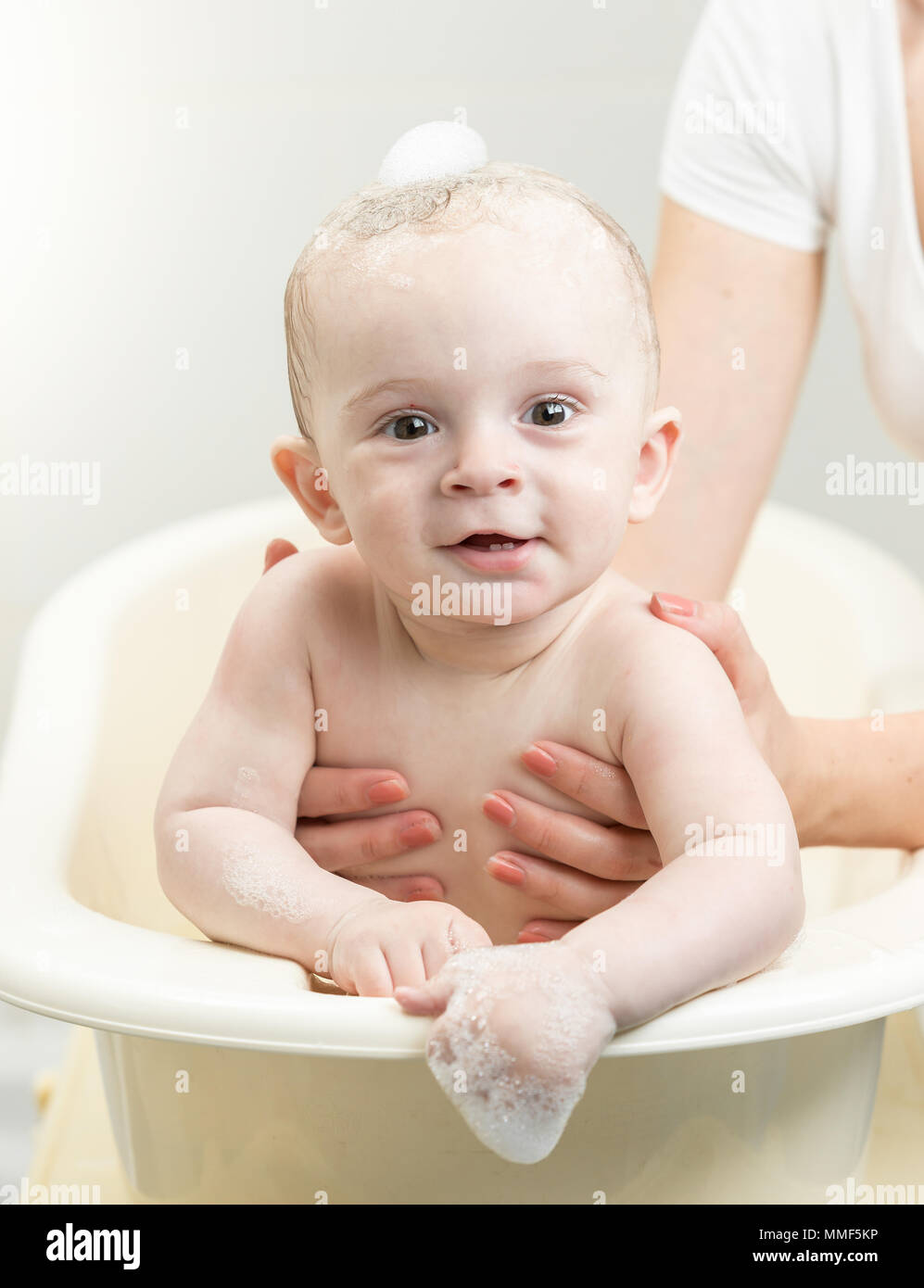 Portrait of cute smiling baby boy washing in bath and looking in camera