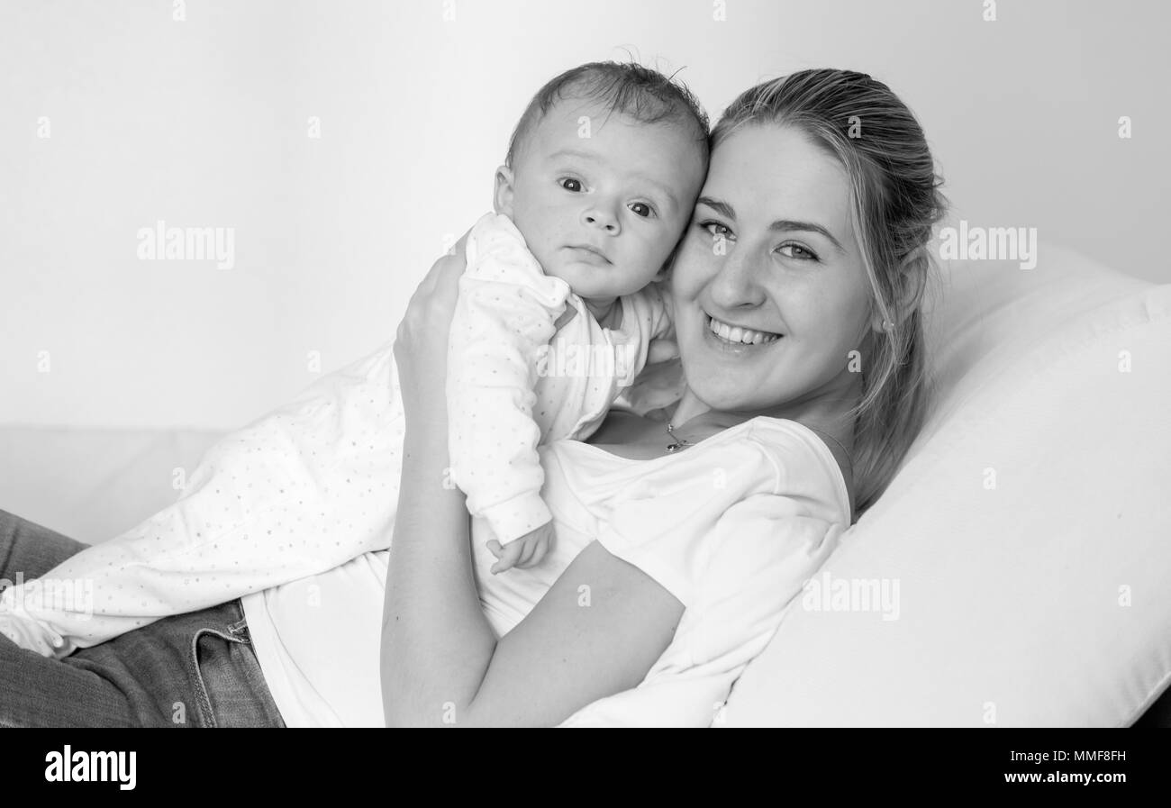 Black and white portrait of smiling young woman lying on bed and holding her 3 months old baby boy Stock Photo