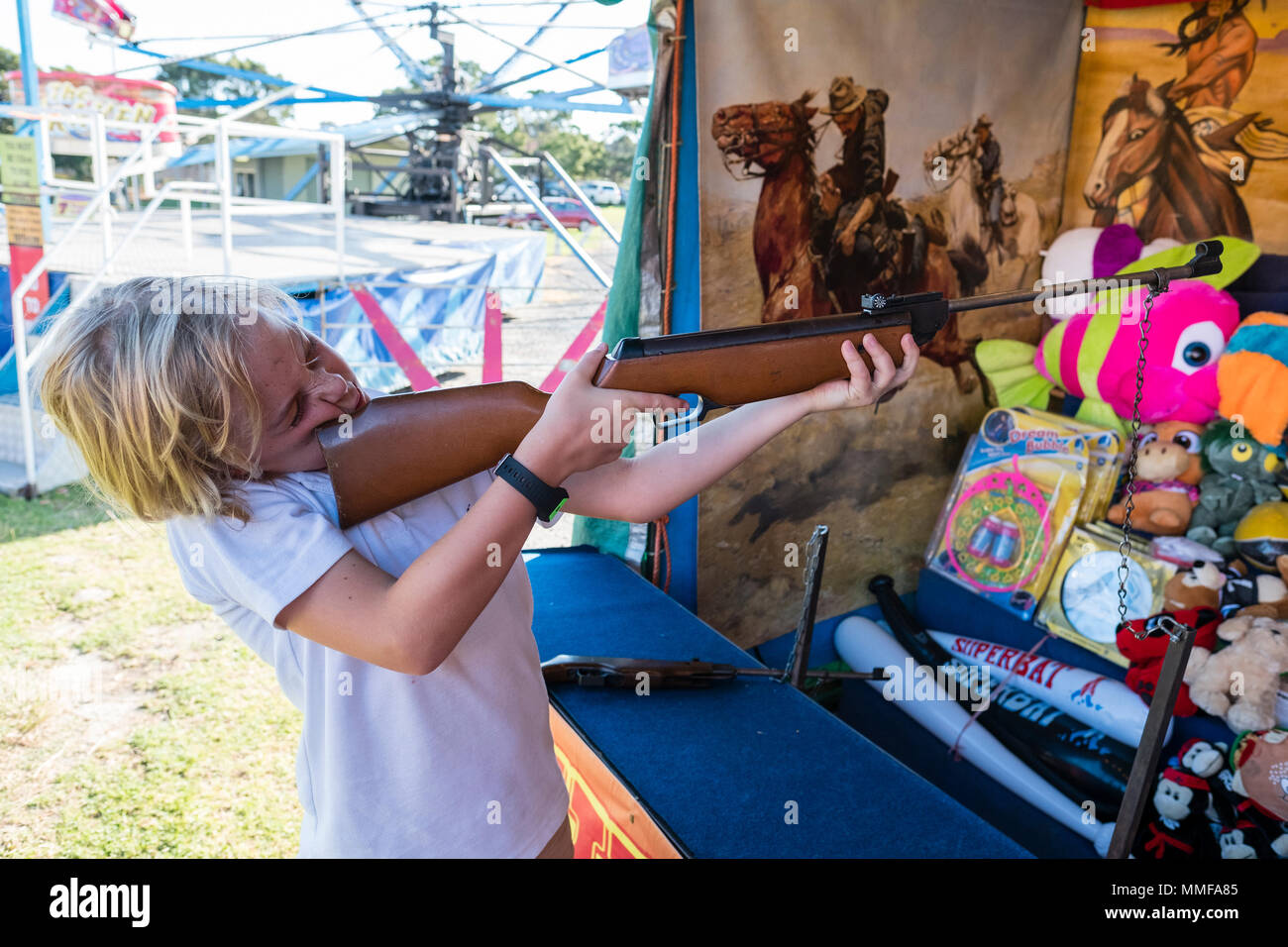 A boy shoots a gun at metal duck in a sideshow at a fair. Stock Photo