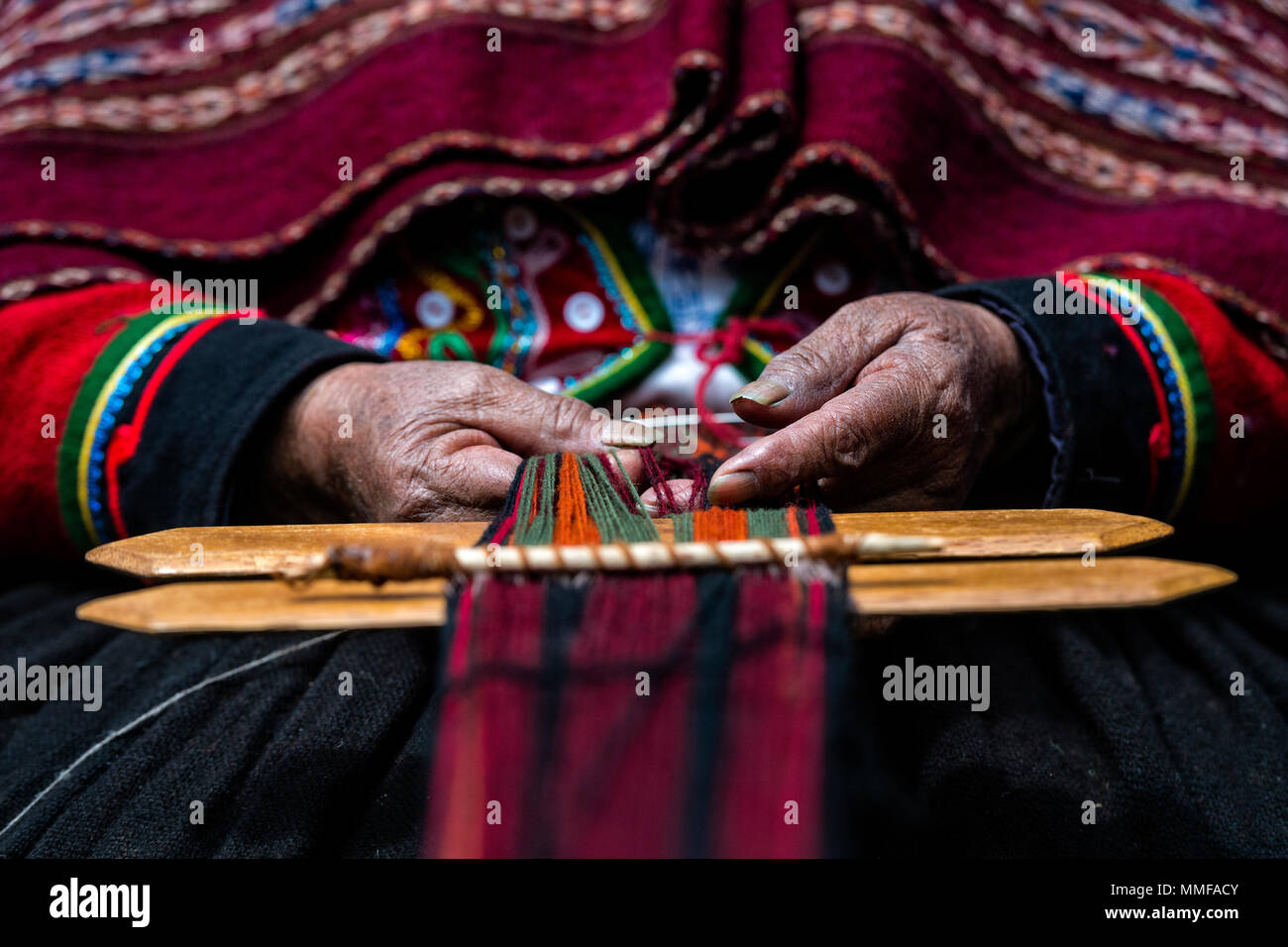 The weathered and hardened hands of an elderly Quechua woman weaving Llama wool. Stock Photo