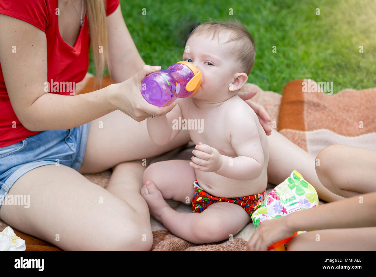 Cute baby boy sitting on blanket on family picnic and drinking juice from bottle Stock Photo