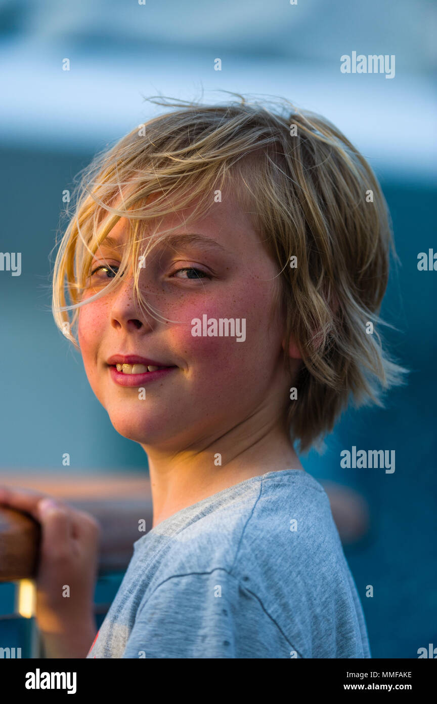A blonde boy watches sunset from the deck of an expedition ship. Stock Photo
