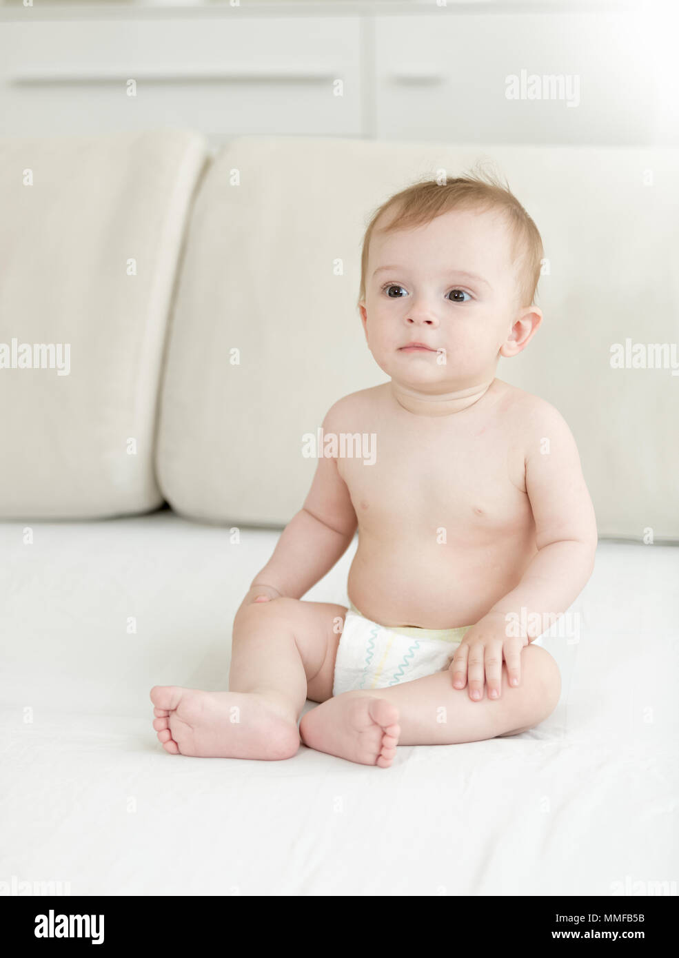 Adorable 10 months old baby boy in diapers sitting on bed Stock Photo