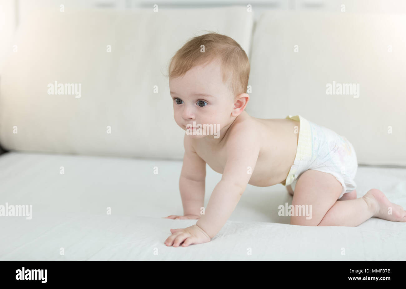 Adorable 10 months old baby boy in diapers crawling on bed Stock Photo