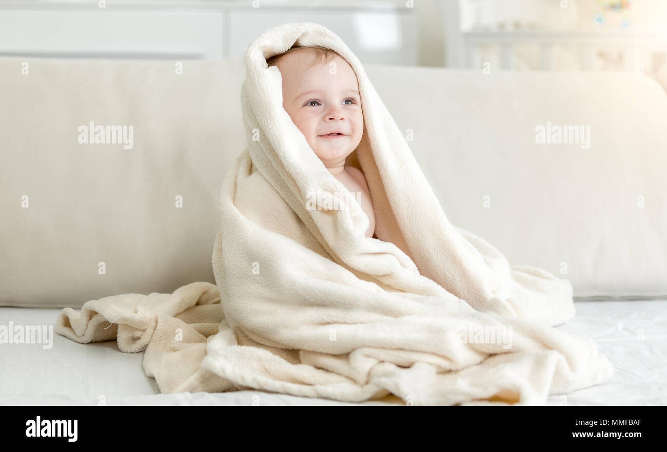 Portrait of cute 10 months old smiling baby boy sitting on bed under