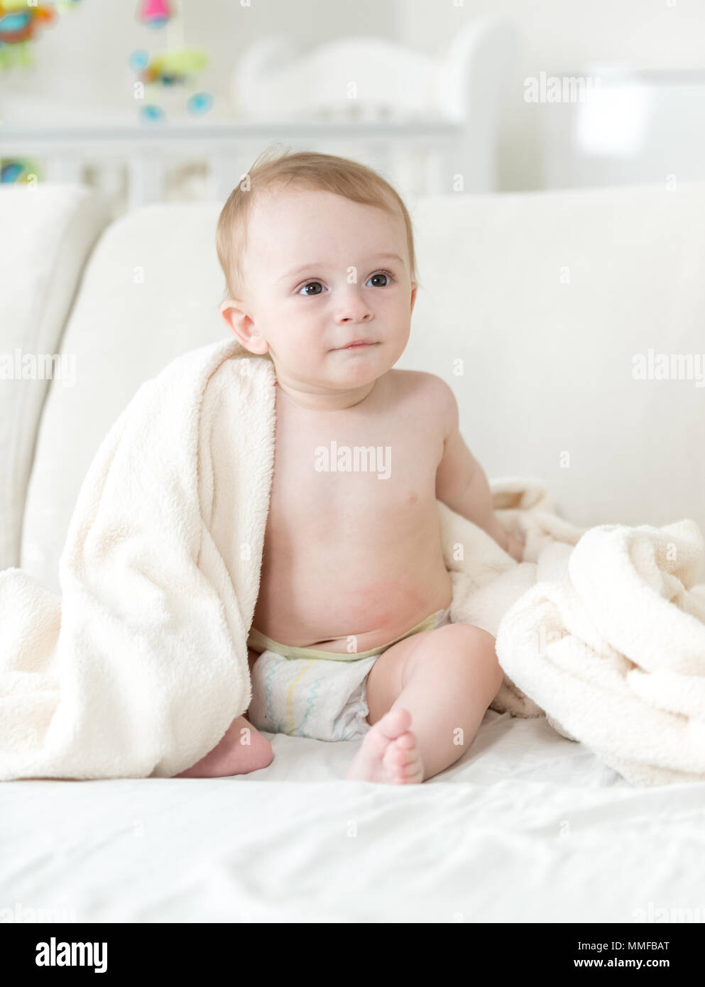 Cute Baby Boy In Diapers Sitting On Sofa And Covering With Blanket