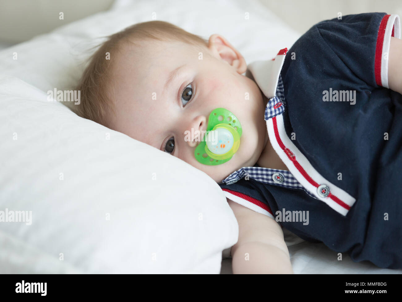 Closeup portrait of 10 months old baby boy lying on pillow and holding