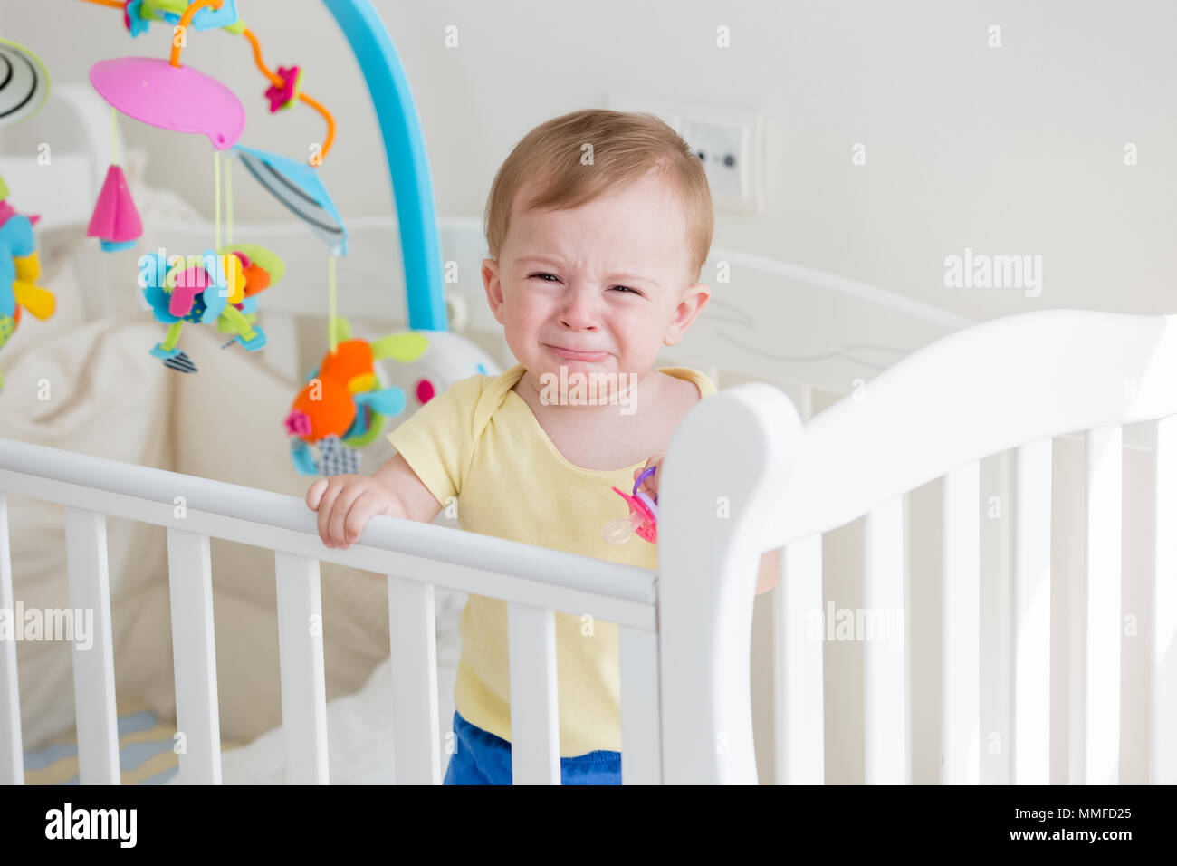 Portriat of 10 months old baby boy standing in cot and crying Stock