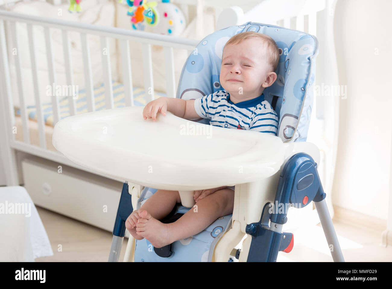10 months old baby boy sitting in highchair and crying Stock Photo