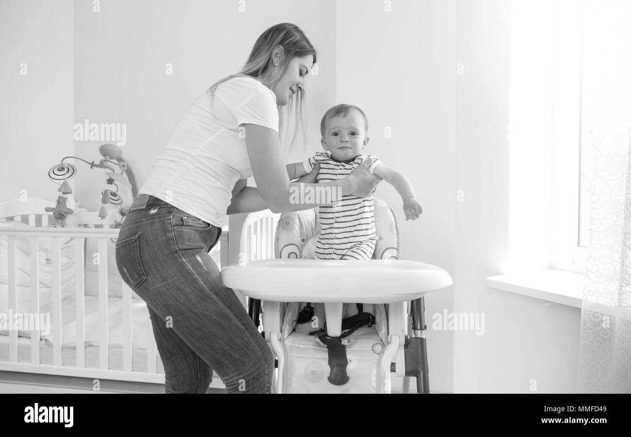 Black and white image of oyung mother seating her baby son in highchair for feeding Stock Photo