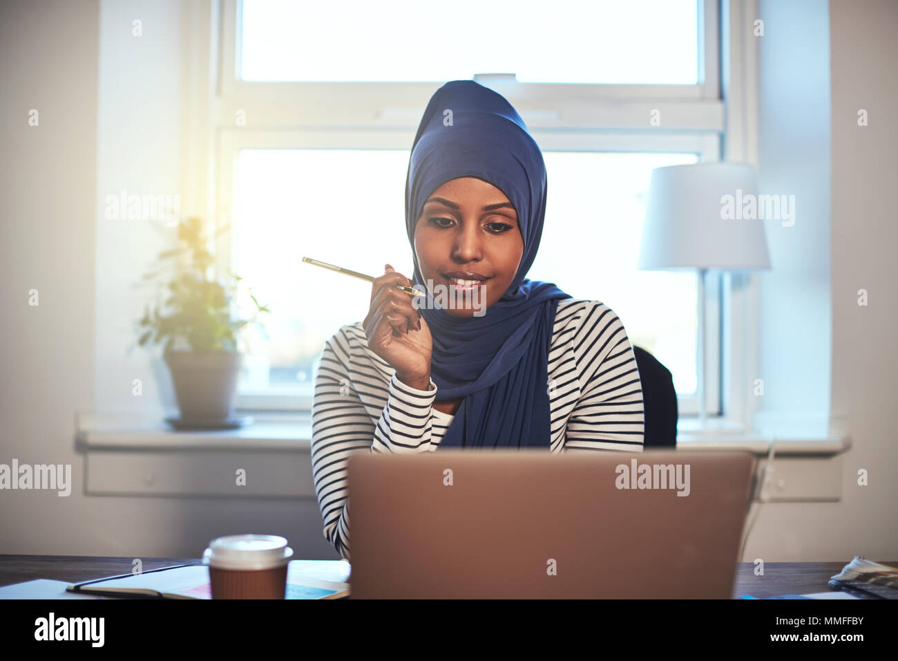 Smiling Arabic female entrepreneur wearing a hijab working online with ...