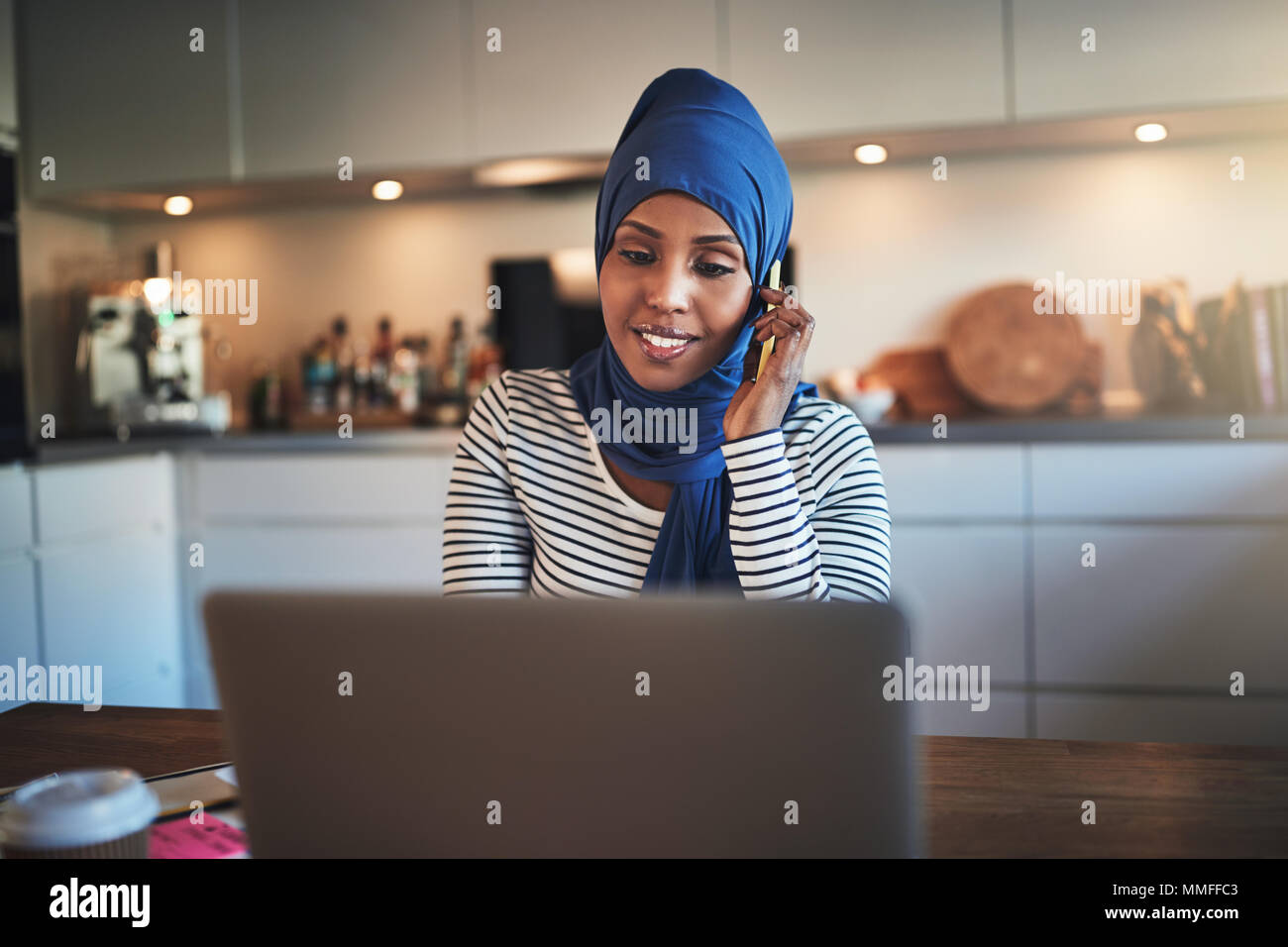 Smiling young Arabic female entrepreneur wearing a hijab sitting at a ...