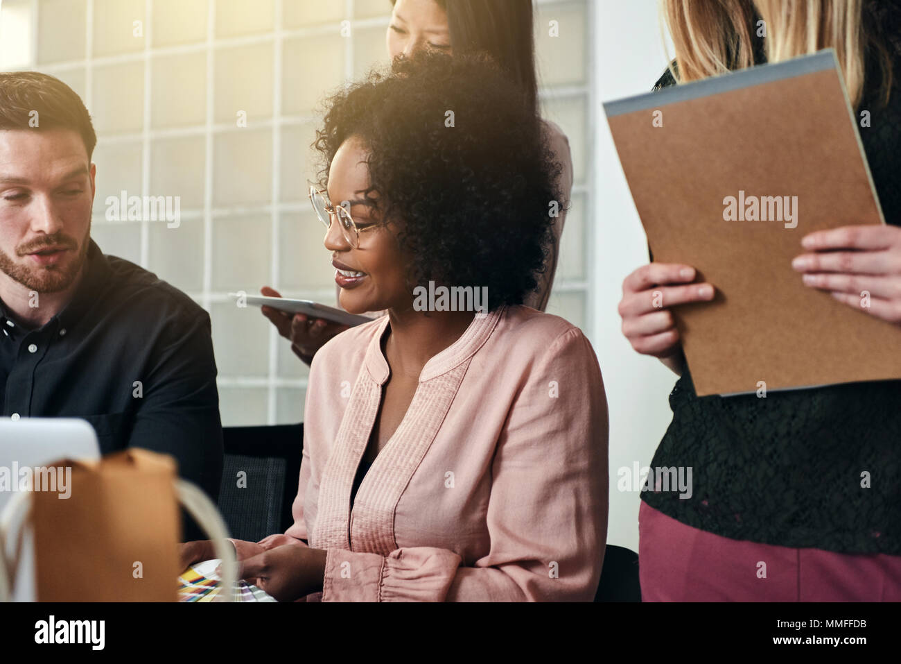 Smiling African businesswoman working at a desk with a diverse group of ...