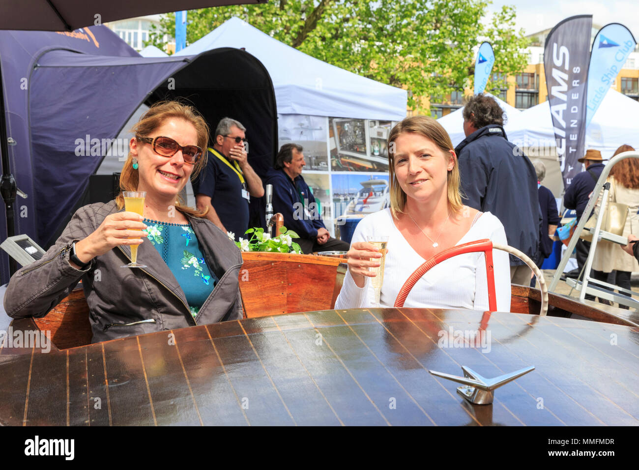 St Katherine Docks, London, 11th May 2018. Two visitors enjoy the sunshine and yachts on display with a glass of Prosecco on a small wooden vessel. Now in its fourth year and held at an iconic marina next to the heart of the City of London and Tower Bridge, London On-Water is an On-Water Boat Show and festival, where yachts, boats, cars and a whole host of other companies can be seen both on the water and on land. It runs from May 10-12. Credit: Imageplotter News and Sports/Alamy Live News Stock Photo