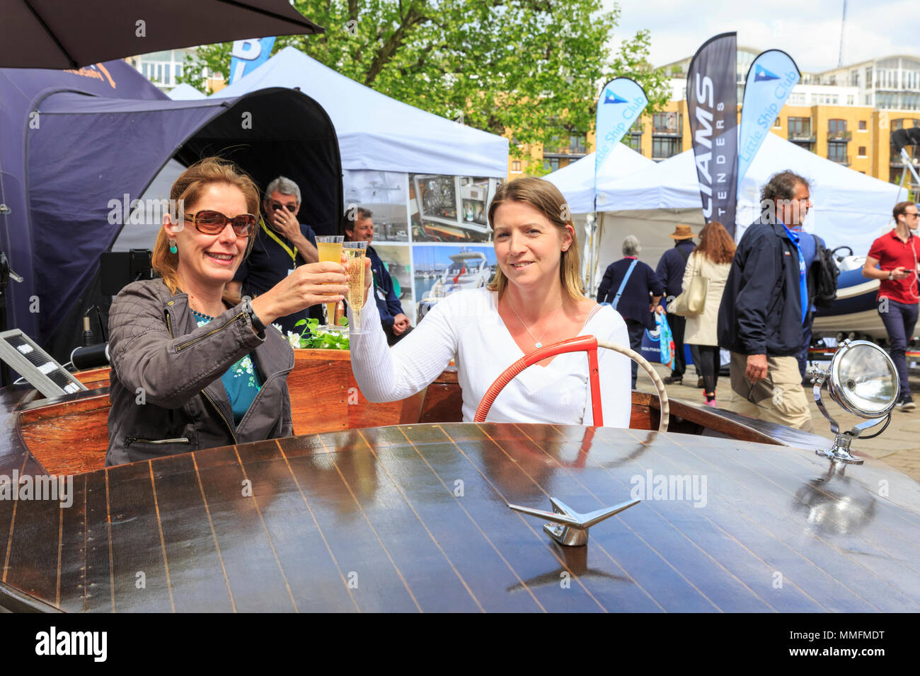 St Katherine Docks, London, 11th May 2018. Two visitors enjoy the sunshine and yachts on display with a glass of Prosecco on a small wooden vessel. Now in its fourth year and held at an iconic marina next to the heart of the City of London and Tower Bridge, London On-Water is an On-Water Boat Show and festival, where yachts, boats, cars and a whole host of other companies can be seen both on the water and on land. It runs from May 10-12. Credit: Imageplotter News and Sports/Alamy Live News Stock Photo