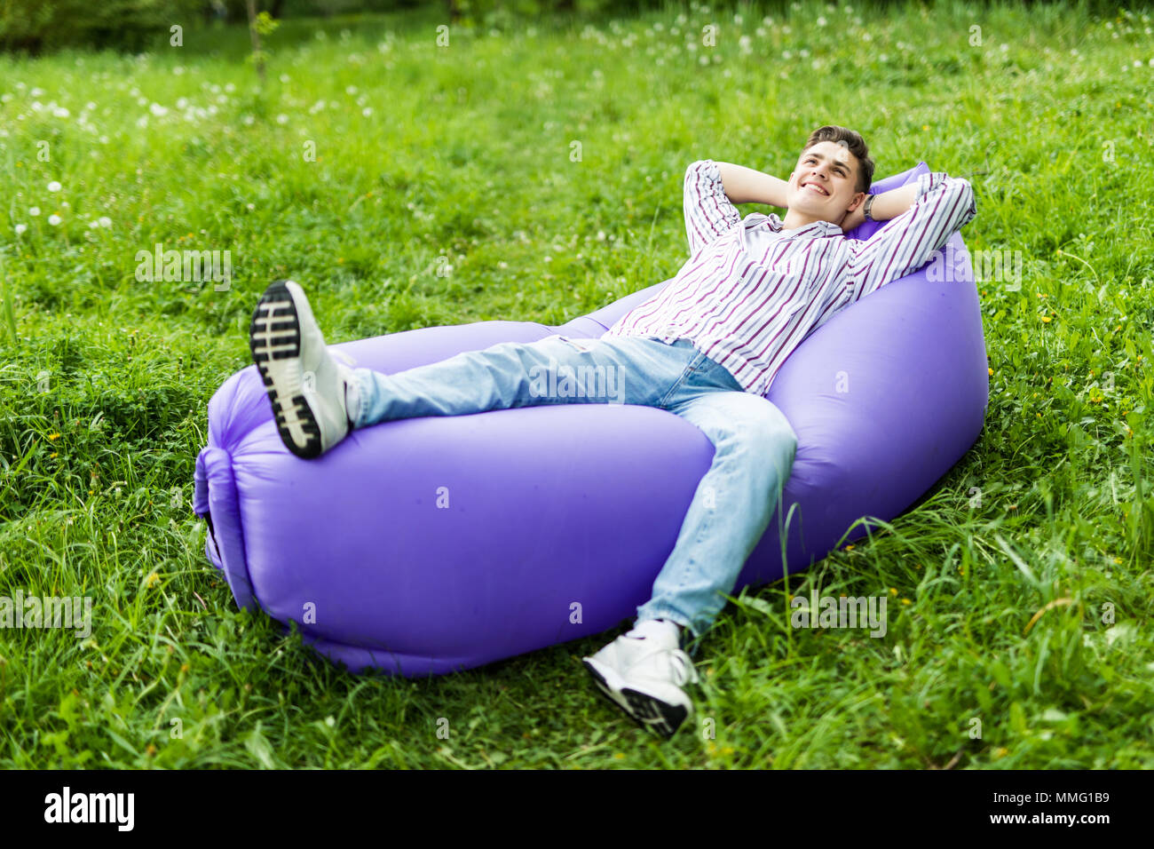 Handsome young man lying on inflatable sofa lamzak while resting on grass in park Stock Photo