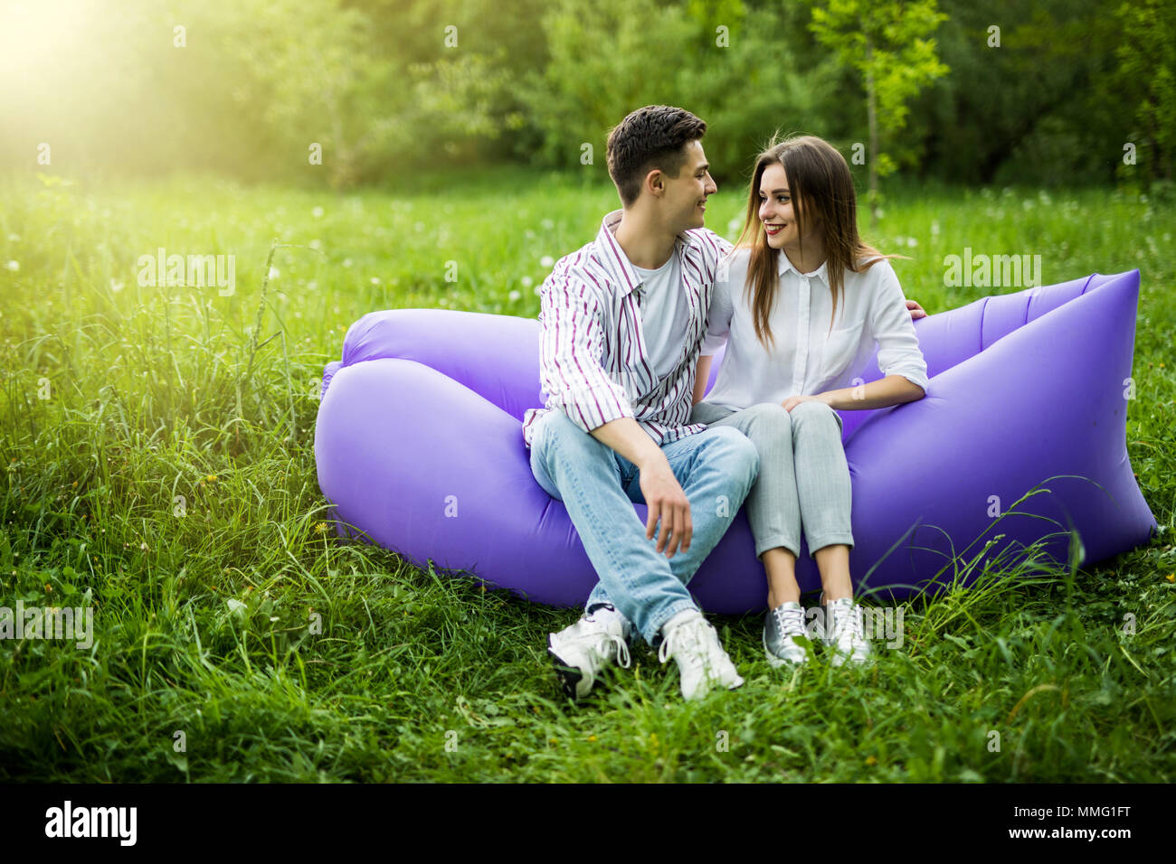 Young couple spend time together sitting on inflatable sofa while resting on grass in park Stock Photo