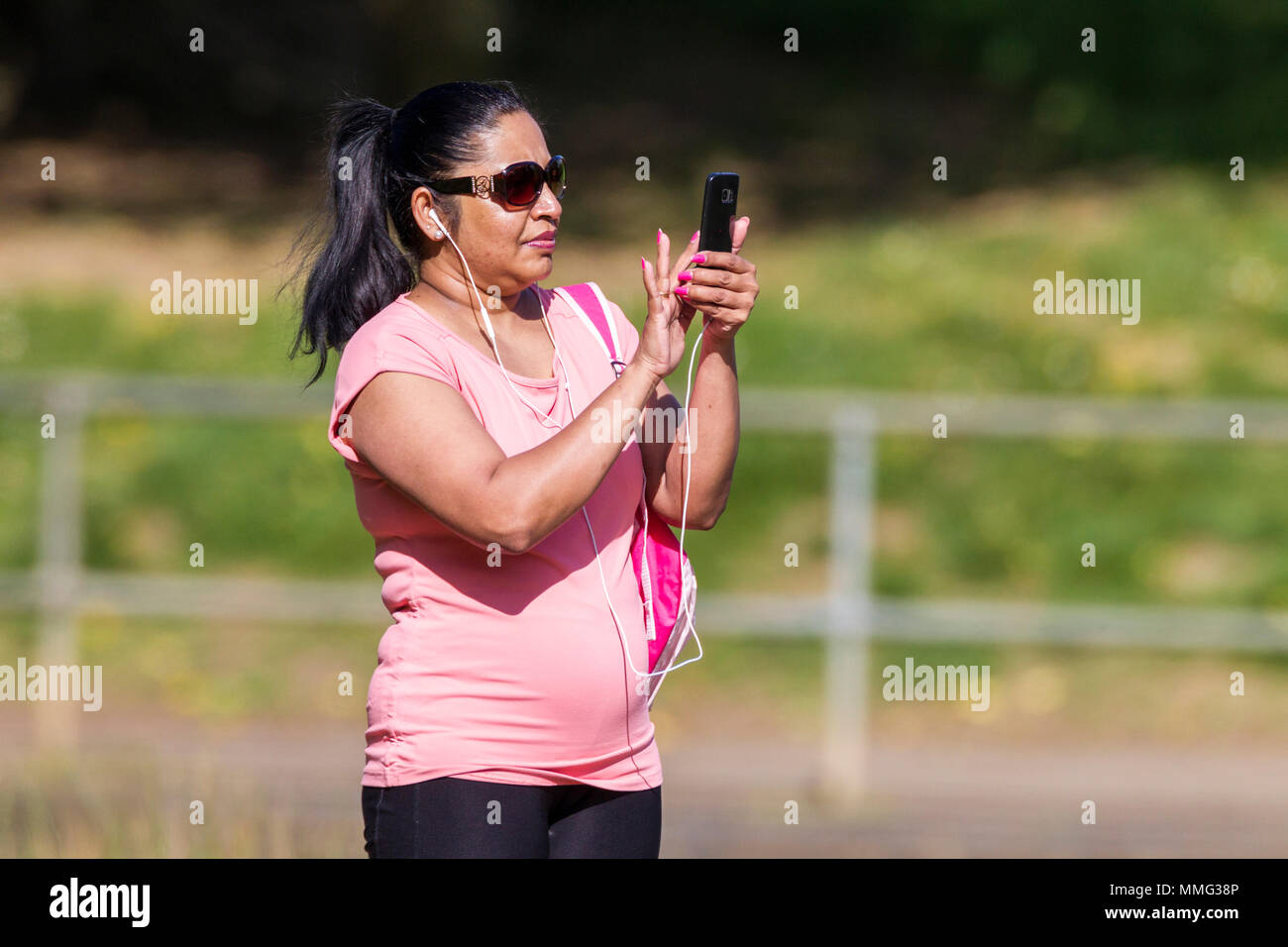 Asian lady taking photographs with her mobile phone in abington Park, Northampton. Stock Photo