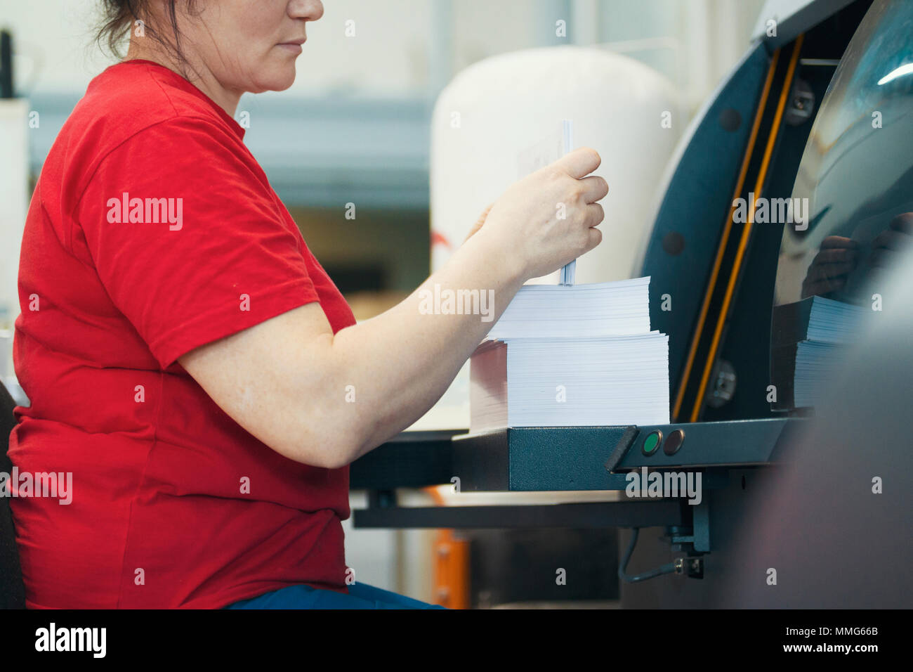 Hands of female worker with a stacks of paper in front of printing machinery equipment Stock Photo